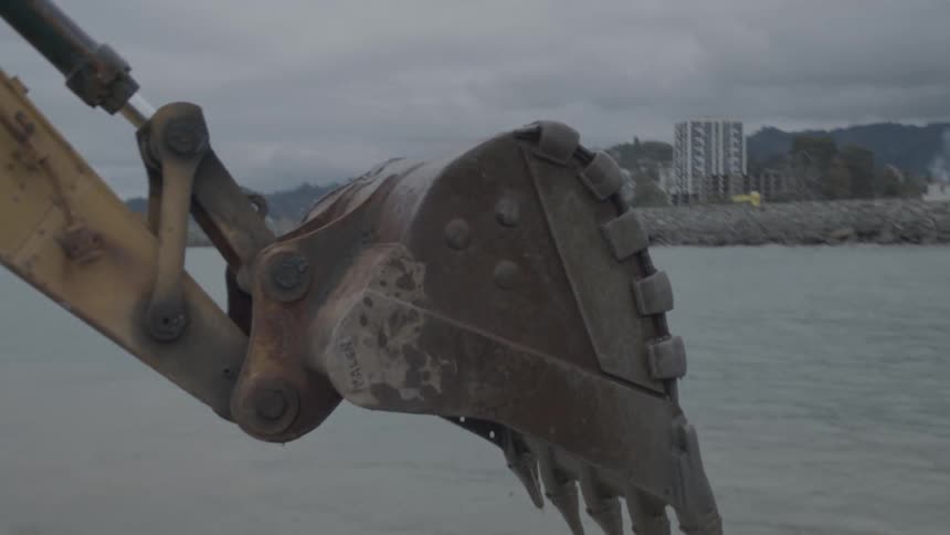 A powerful excavator scoops up rocks from the ocean floor in slow motion to build a coastal barrier