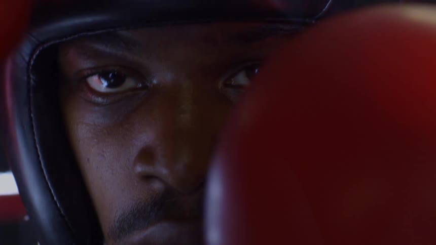 An intense close-up of a determined boxer in headgear staring down the camera before his glove covers the lens
