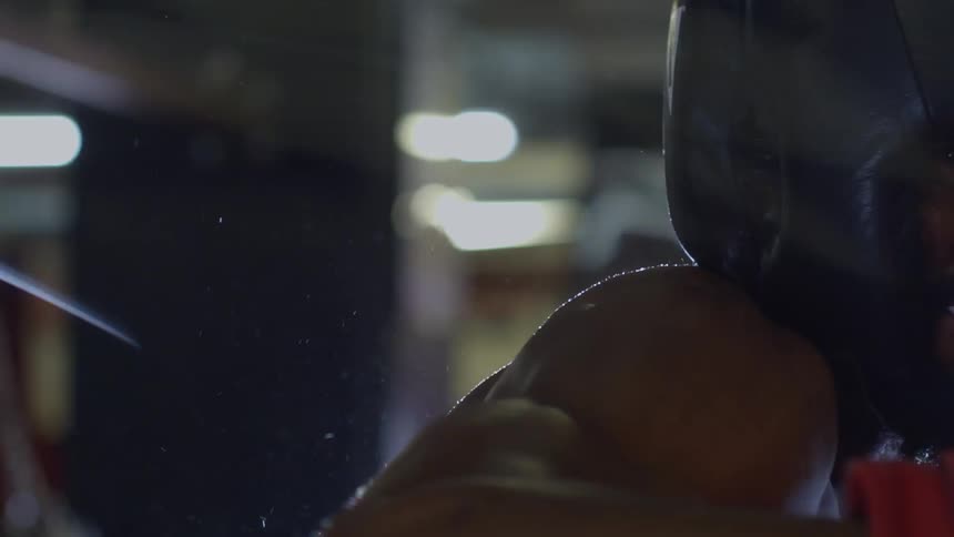 An intense boxer in headgear trains hard in a dimly lit gym, with sweat flying in dramatic slow motion