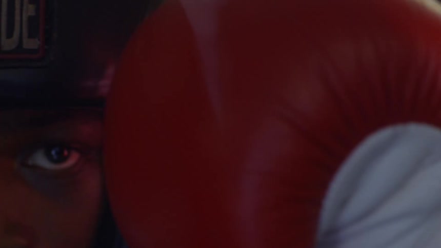 An extreme close-up of a focused boxer's eye peering over a red boxing glove in a defensive stance