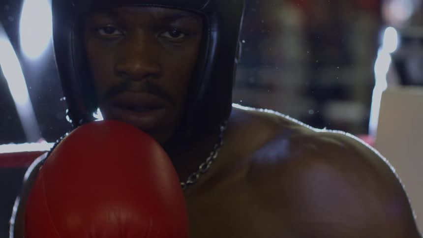 An intense slow motion close-up of a determined boxer staring forward as a bright lens flare washes over the screen
