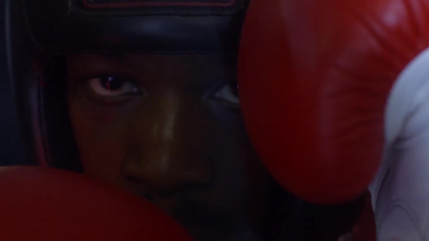 A determined boxer in protective headgear stares down his opponent with intensity in an extreme close-up slow-motion shot