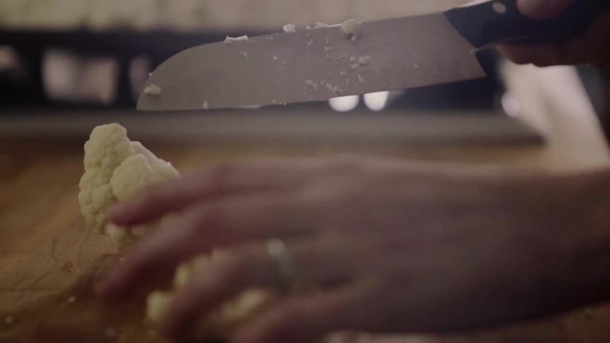 A woman is using a knife to cut cauliflower