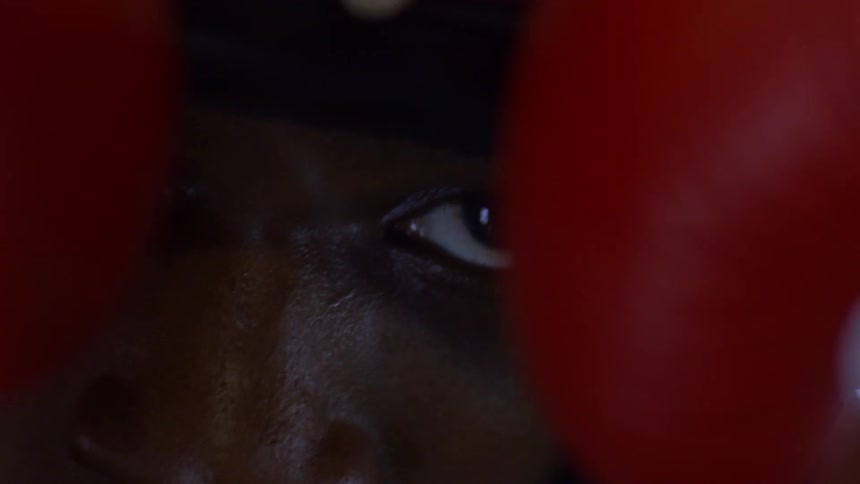 An extreme close-up of a focused boxer's eye, peering through his red boxing gloves with intense determination