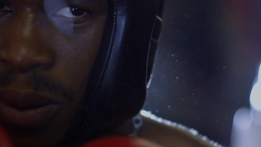 A cinematic slow-motion extreme close-up of a determined male boxer's face as he stares intensely at the camera