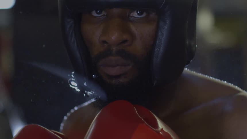 An intense boxer in a head guard stares directly into the camera in dramatic slow motion