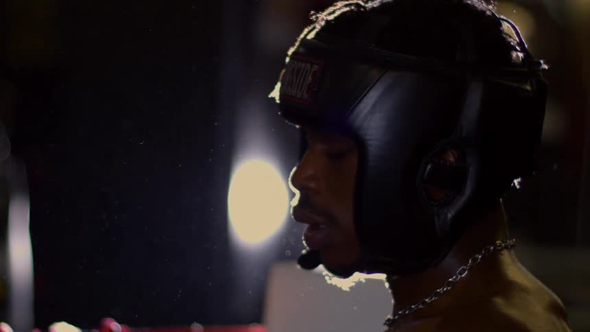A dramatically lit boxer in headgear catches his breath in slow motion, with dust particles floating in the air