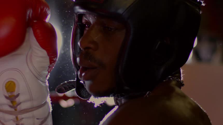 A sweaty boxer in headgear breathes heavily in the ring in a dramatic slow motion close-up