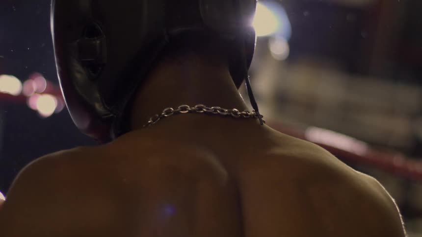 A slow motion, over-the-shoulder shot reveals a boxer's back as he stands in the ring under a single spotlight