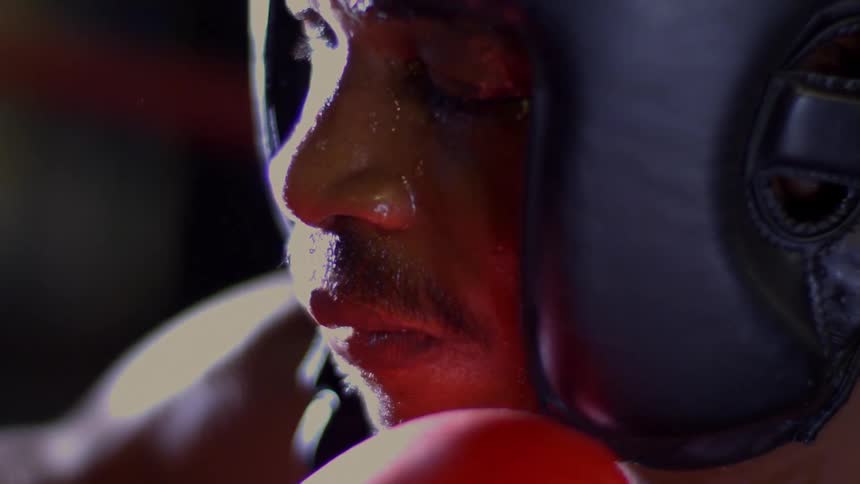An extreme close-up shot shows a sweaty, defeated boxer wearing protective headgear and gloves