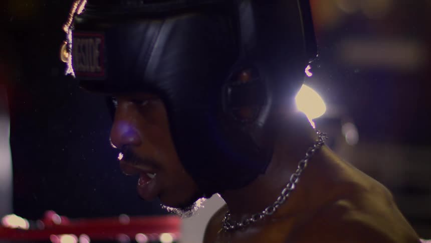 Intense slow-motion profile shot of a boxer with headgear breathing heavily in a dimly lit gym