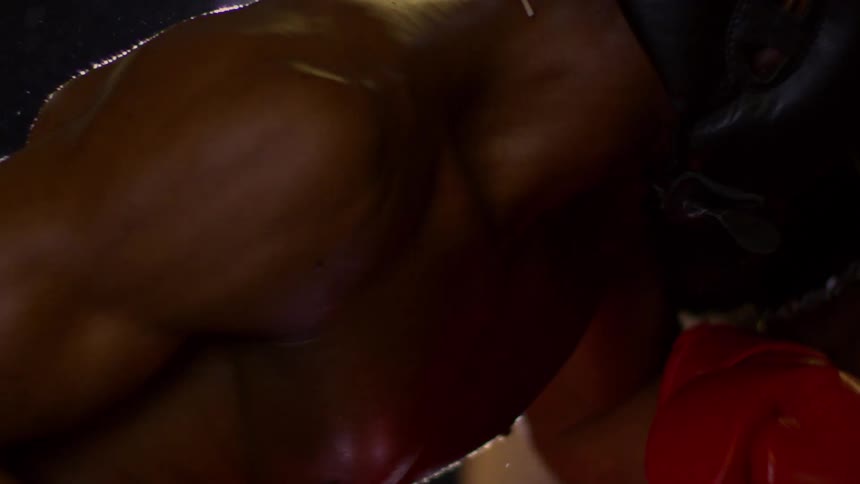 Two muscular boxers spar in slow motion as a red glove makes powerful contact with a fighter's black headgear