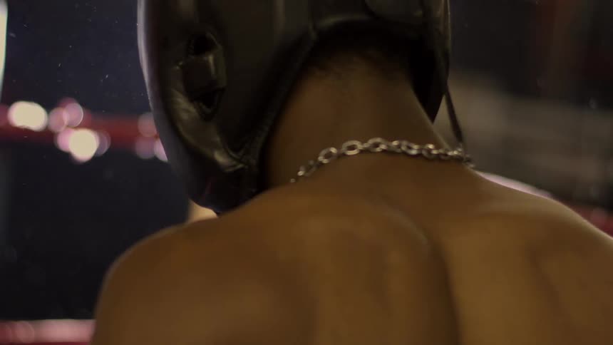 Cinematic close-up from behind a boxer in headgear standing in a dark ring under a bright, flaring light