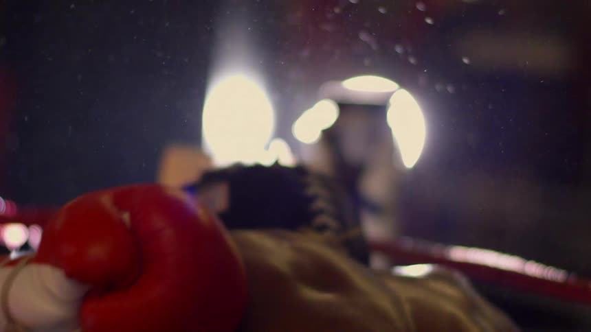 A dramatic slow-motion close-up of a sweaty boxer's muscular back as he recovers in the ring