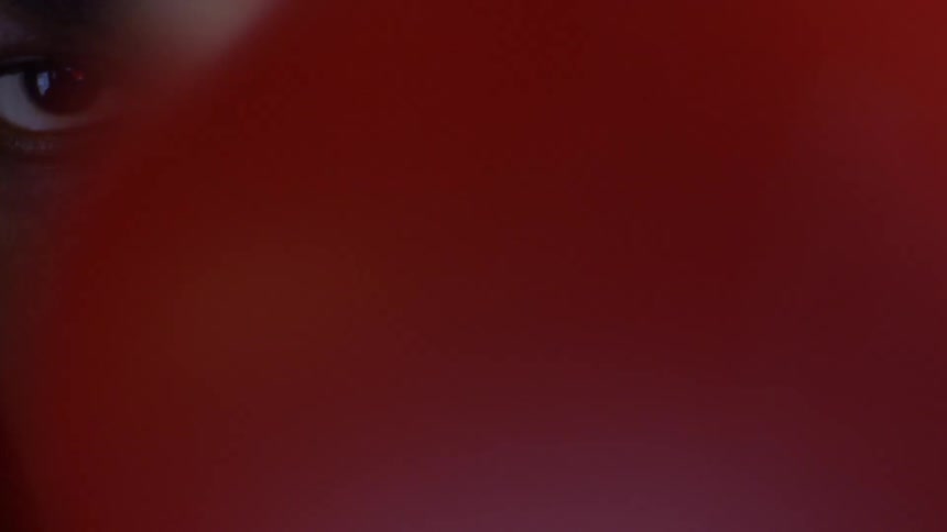 An intense close-up of a Black man's eyes emerges from a colorful, blurry background with moody lighting