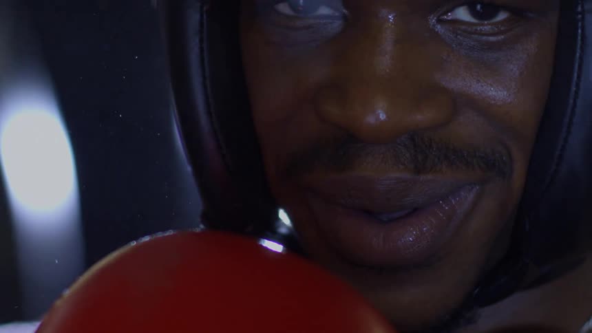 A close-up slow-motion shot of a focused boxer in headgear whose intense stare turns into a confident and intimidating smile