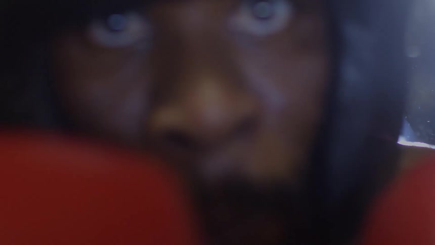 A boxer's intense stare is captured in a blurry, stylistic close-up before the camera is covered by a red glove