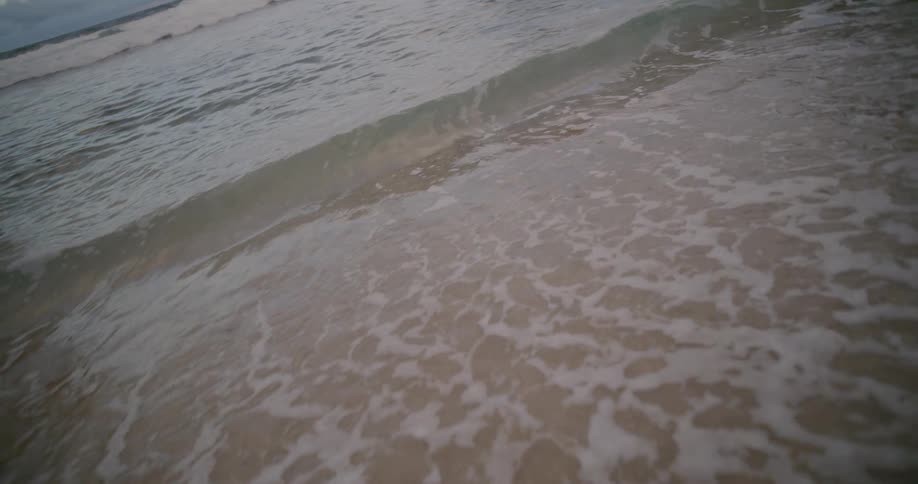 A serene slow-motion close-up of a gentle ocean wave washing over the sandy shore