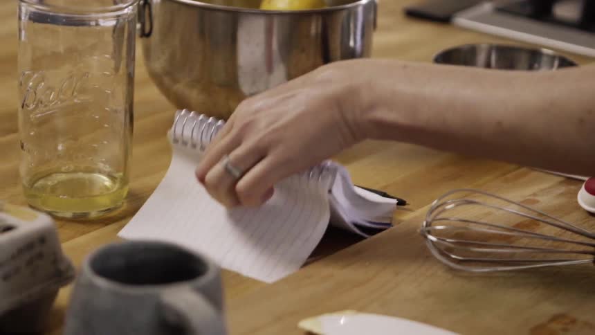 A woman picks up a notebook by a stove