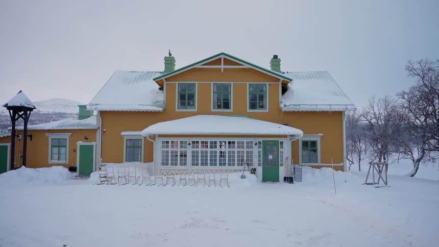 A large yellow house stands in a deep snowy landscape on a cold winter day