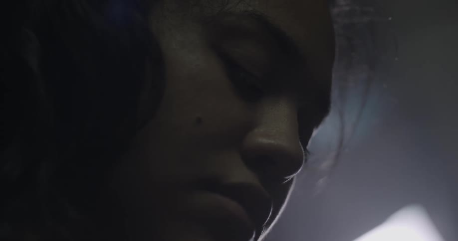 A woman blinks while looking down in a dim room