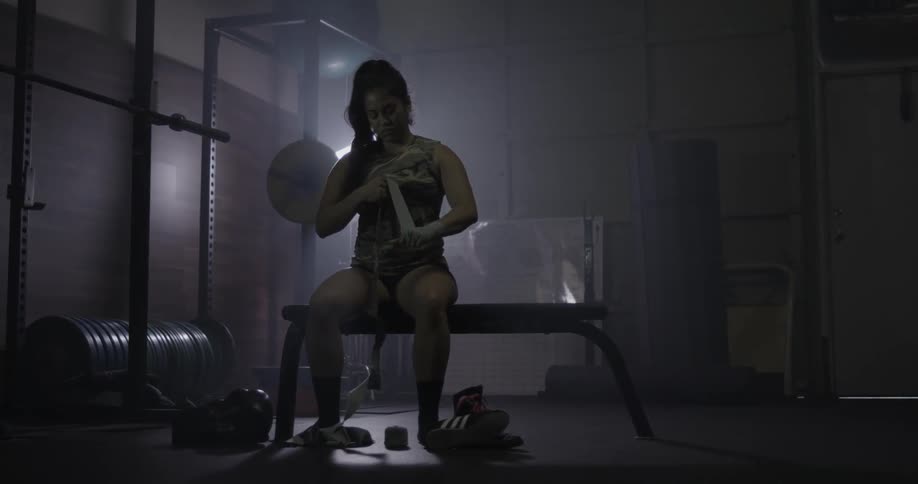 Woman sits on a bench in a gym and wraps wrist
