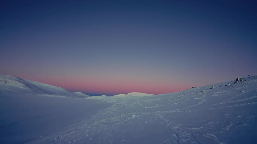 A vast, snowy mountain landscape is bathed in the beautiful pink and purple glow of twilight