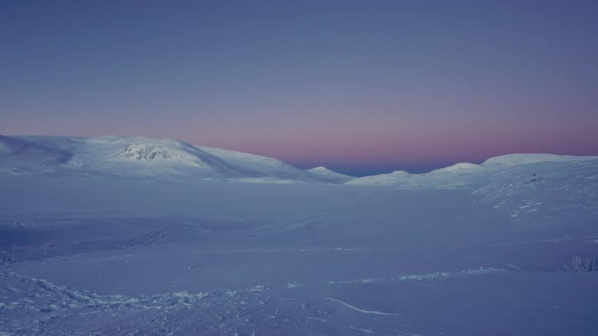A tranquil and wide shot of a vast snowy mountain landscape during a colorful twilight