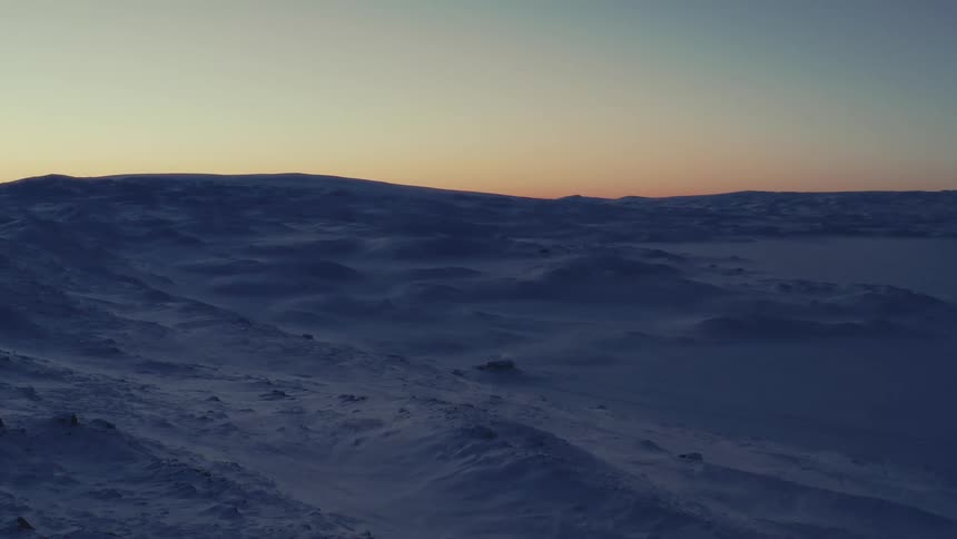 A static wide shot of a vast and desolate snow-covered landscape during a serene twilight