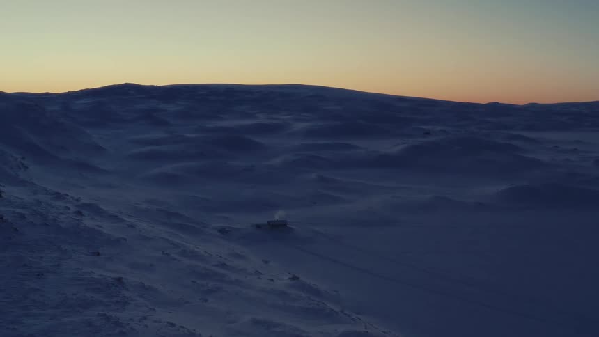 A lone cabin emits smoke from its chimney, nestled in a vast and desolate snow-covered landscape at dusk