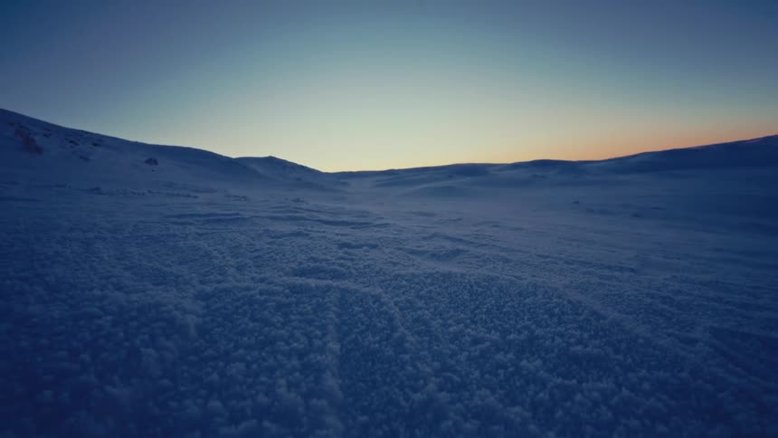 Slowly moving across a vast, untouched snowy landscape during a tranquil winter sunset