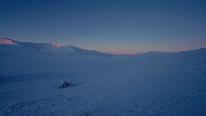 A serene and expansive snowy mountain landscape glows with the pink and blue hues of dawn or dusk
