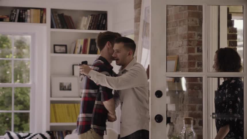 Two men greet and hug and a woman walks up behind them