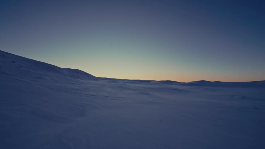 A serene, static shot of a vast snowy mountain landscape during the tranquil twilight hour
