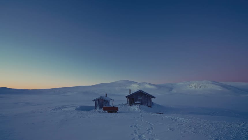 Peaceful twilight descends over two remote wooden huts in a vast, snow-covered Arctic landscape
