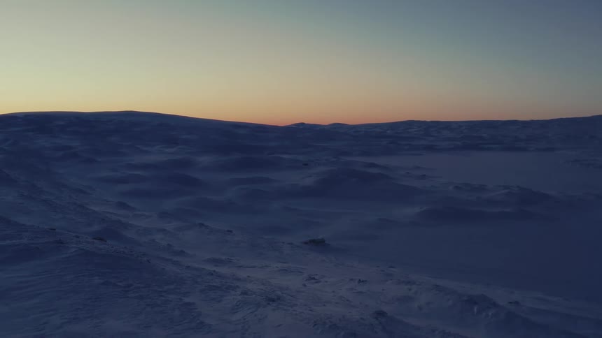 A tranquil and wide shot captures a vast, snow-covered arctic tundra during the twilight hours of sunrise