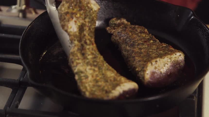 Meat gets turned over with tongs in a frying pan
