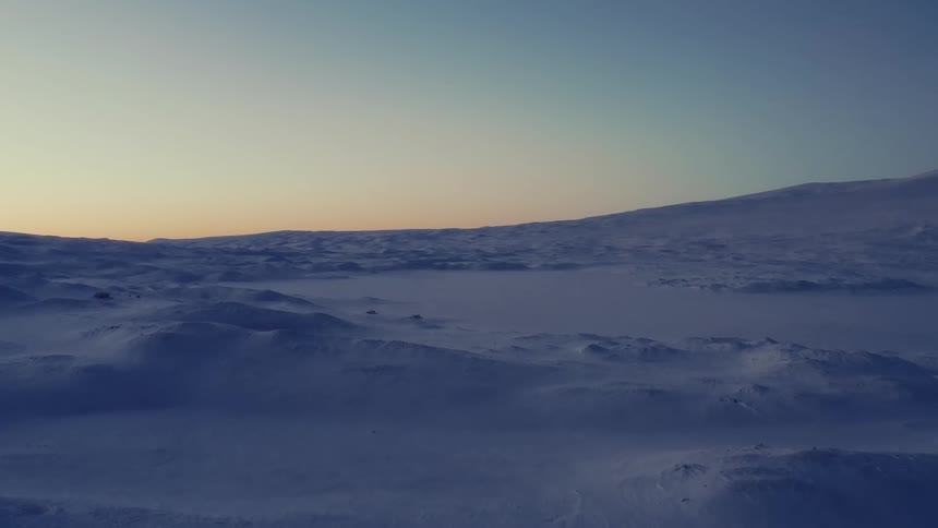 A cold, expansive snow-covered landscape under a serene twilight sky
