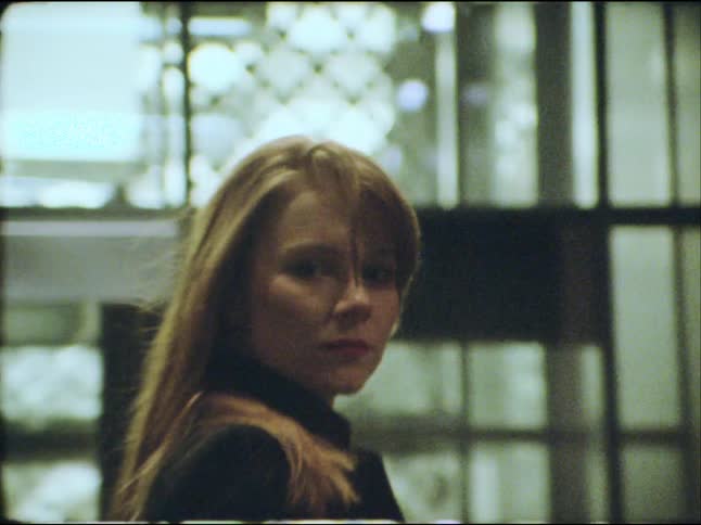 A mysterious woman dramatically whips her long blonde hair in slow motion and stares intently at the camera in a grainy, vintage-style shot