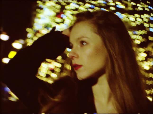 A contemplative woman runs her hand through her hair at night with a backdrop of beautiful city lights