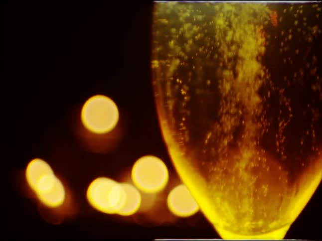 Sparkling champagne bubbles rise in a glass against a backdrop of warm, out-of-focus festive lights at night