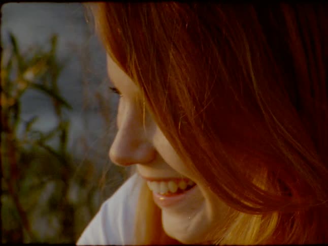 A beautiful young woman with long red hair smiles and laughs happily in the warm golden hour light