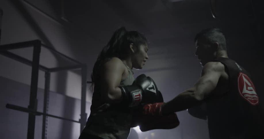 A female fighter and her trainer practice in a gym