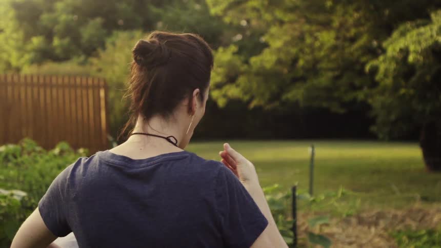 A woman tastes a vegetable from a garden she is working in