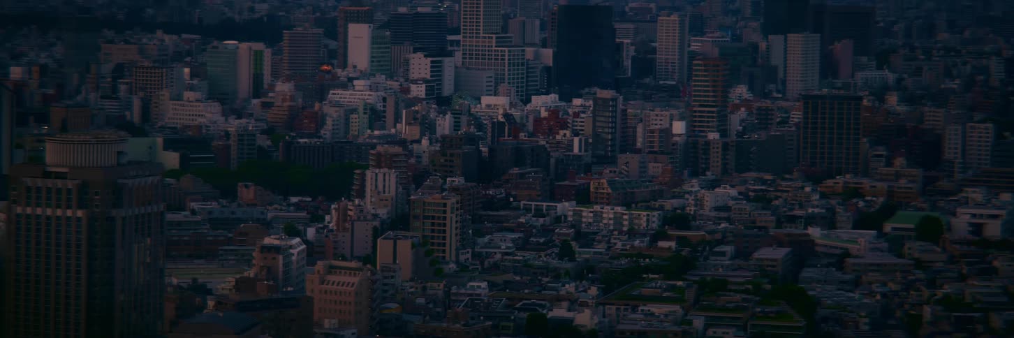 A high-angle timelapse captures the transition from dusk to night over a sprawling, dense cityscape as building lights begin to turn on