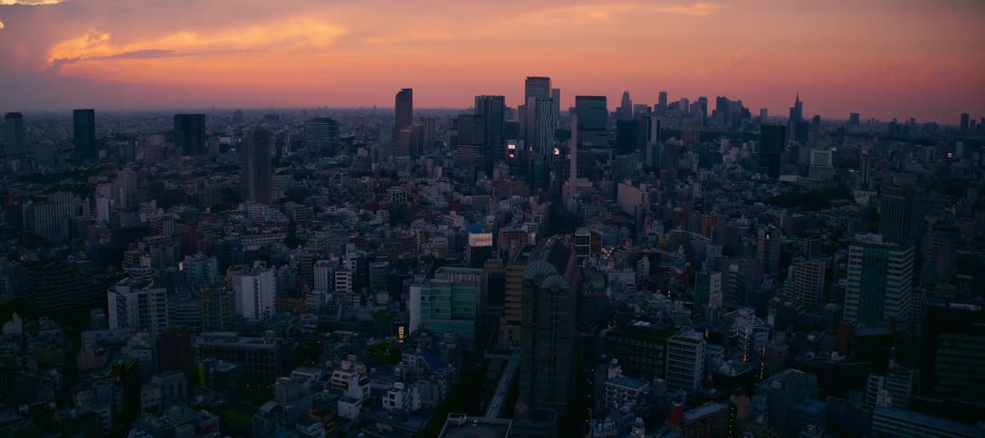 The sprawling skyline of a massive city is cast in silhouette against a brilliant orange and purple sunset