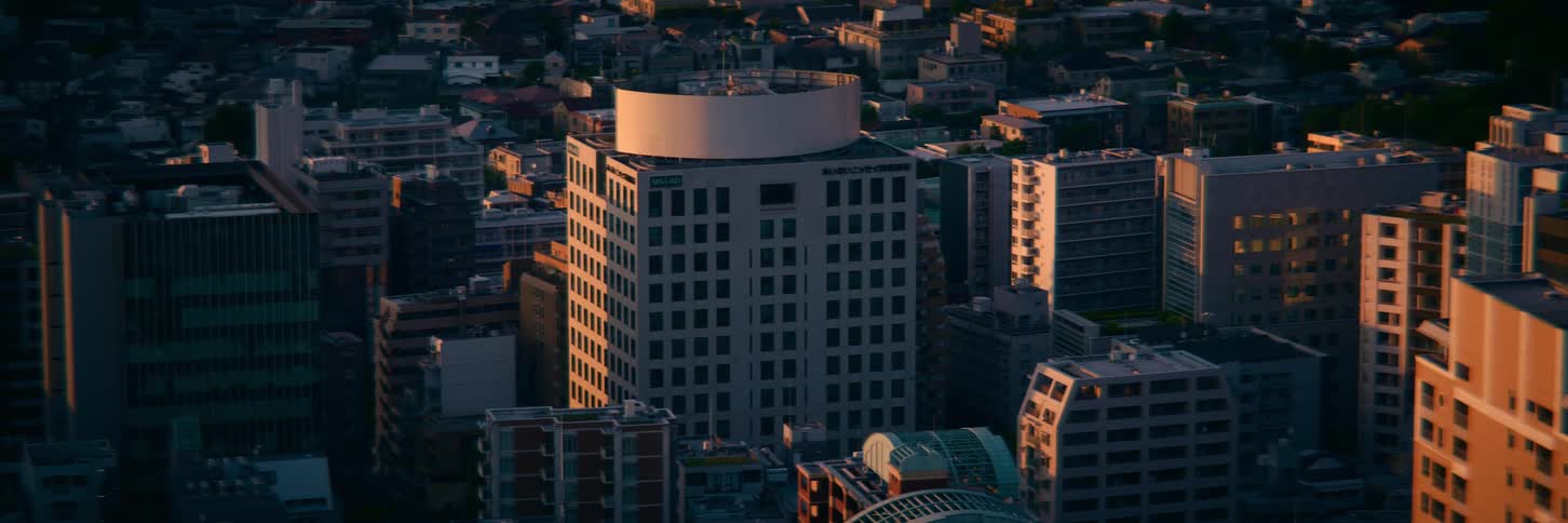 A static high-angle shot captures the sunrise illuminating a modern building amidst a dense cityscape