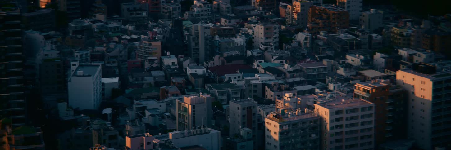 A static high-angle shot of a dense cityscape in Tokyo, with warm sunset light hitting the tops of buildings