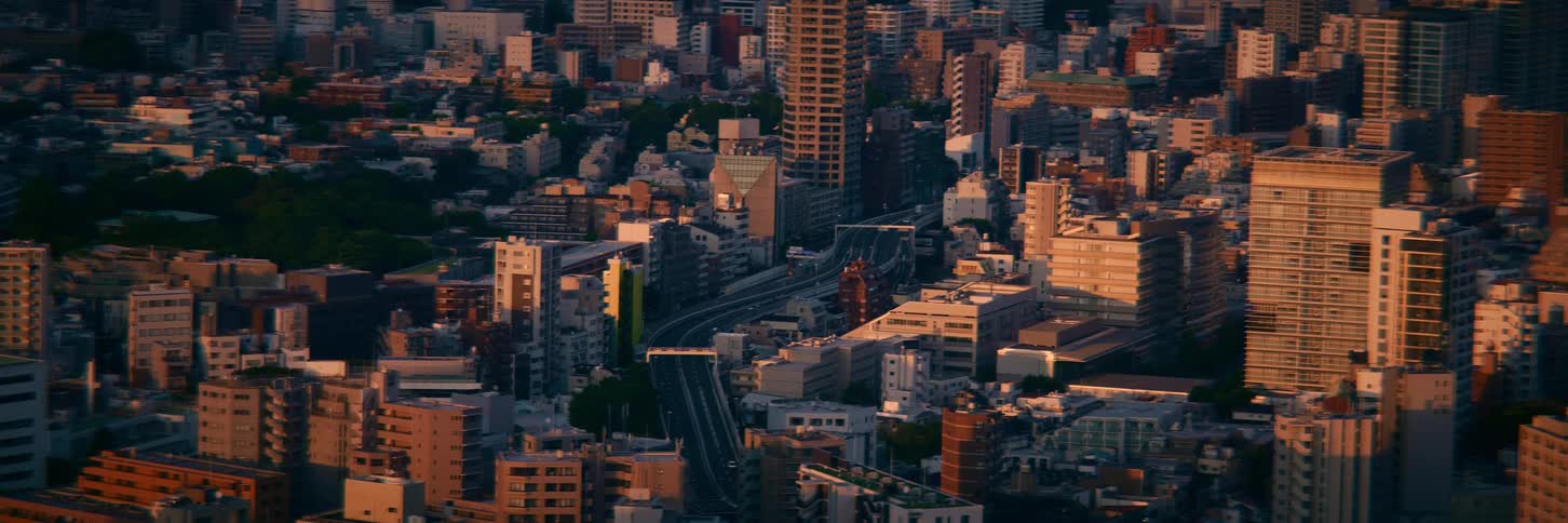 Golden hour sunset light illuminates a vast, dense cityscape with a busy highway weaving through the urban sprawl
