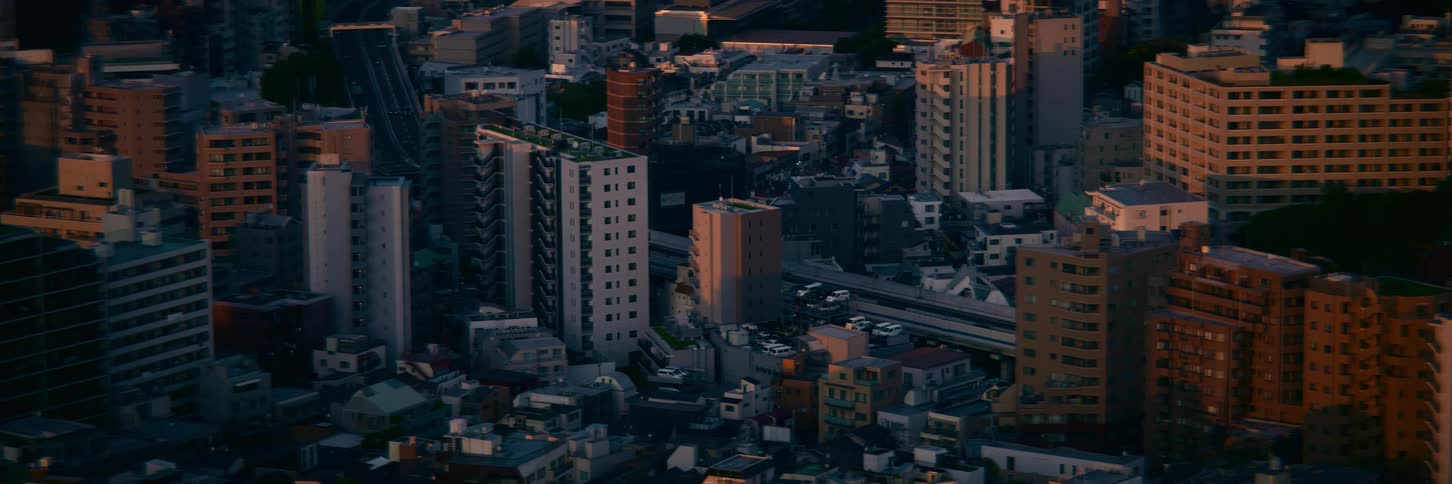 Static aerial shot of a dense Tokyo cityscape with traffic flowing along a highway during a dramatic golden hour sunset